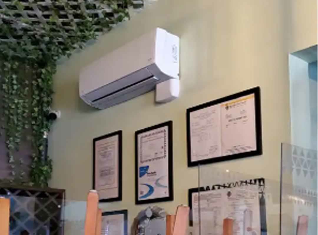 A mini-split mounted high on the wall of a small cafe dining room, above a row of framed certificates